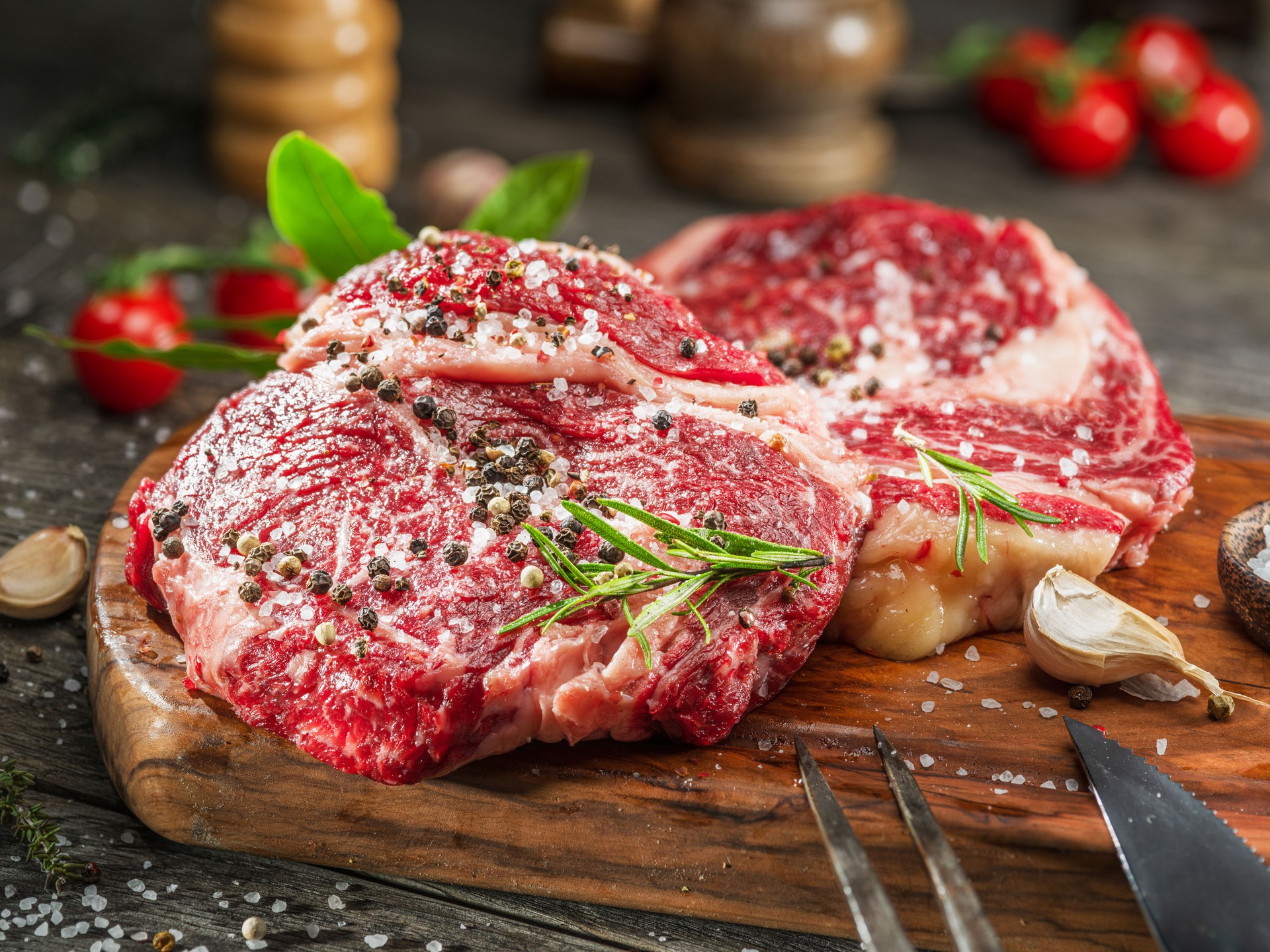 Raw beef steaks with herbs and spices ready for cooking are on wooden board.