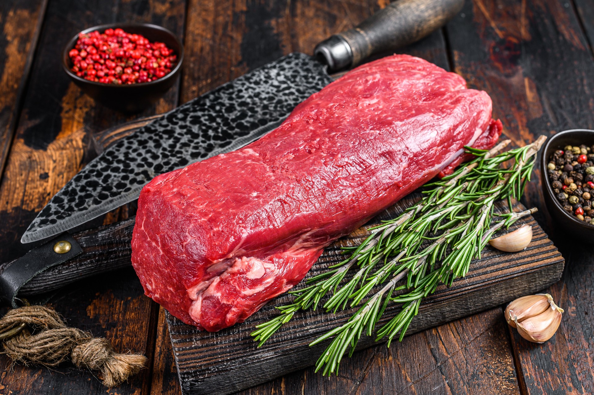 Whole Raw Tenderloin beef meat for steaks fillet mignon on a wooden cutting board with butcher knife. Dark  wooden background. Top view